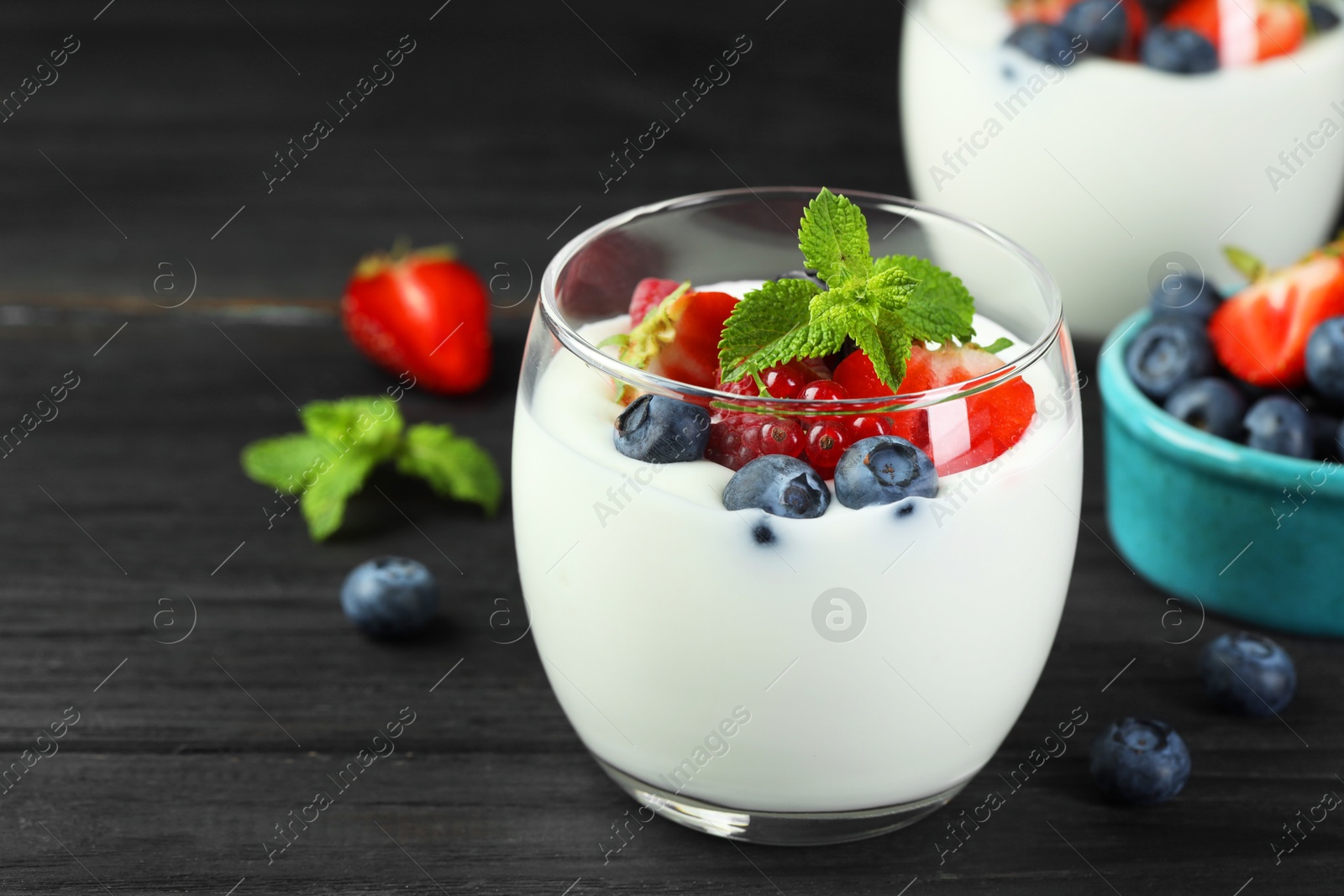 Photo of Tasty yogurt with fresh berries and mint in glasses on black wooden table, closeup