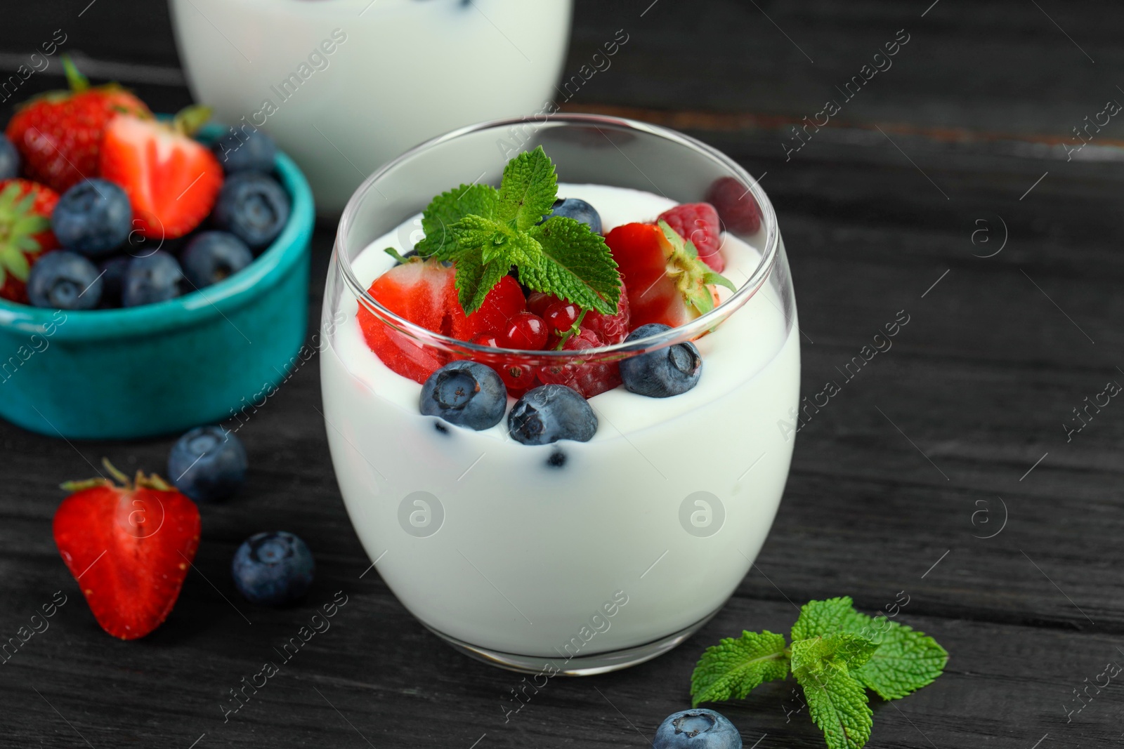 Photo of Tasty yogurt with fresh berries and mint in glass on black wooden table, closeup