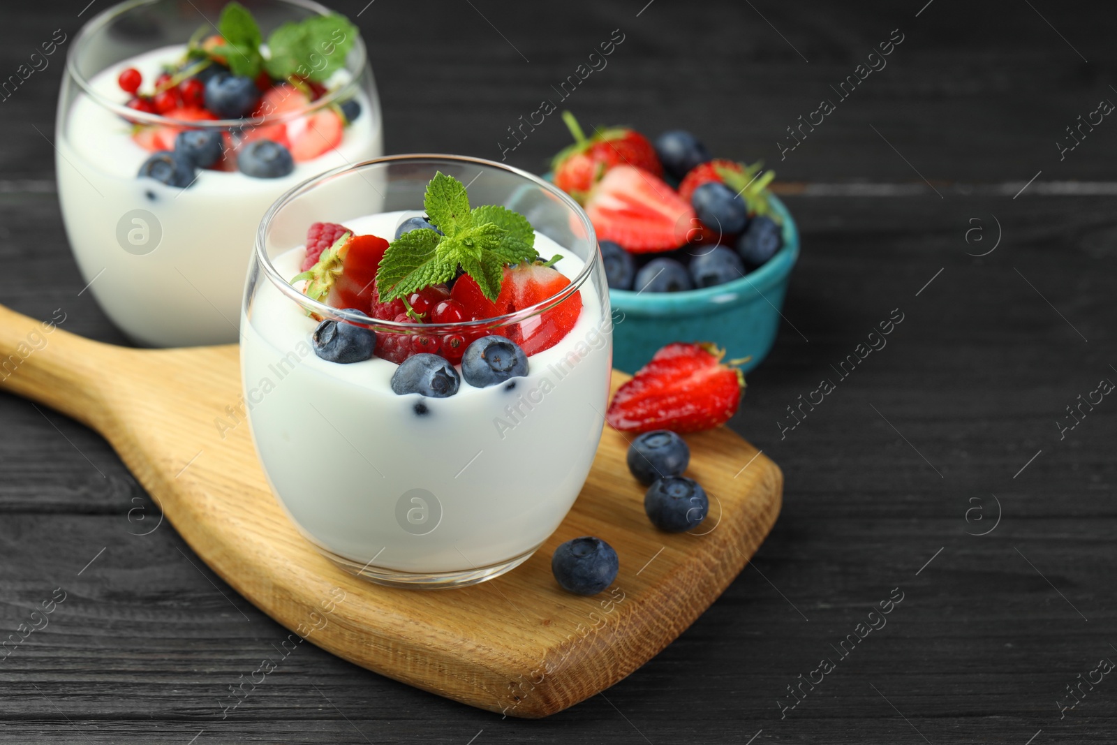 Photo of Tasty yogurt with fresh berries and mint in glasses on black wooden table, closeup