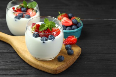 Photo of Tasty yogurt with fresh berries and mint in glasses on black wooden table, closeup