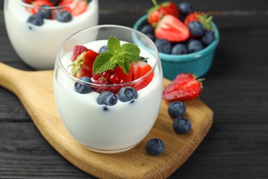 Photo of Tasty yogurt with fresh berries and mint in glasses on black wooden table, closeup