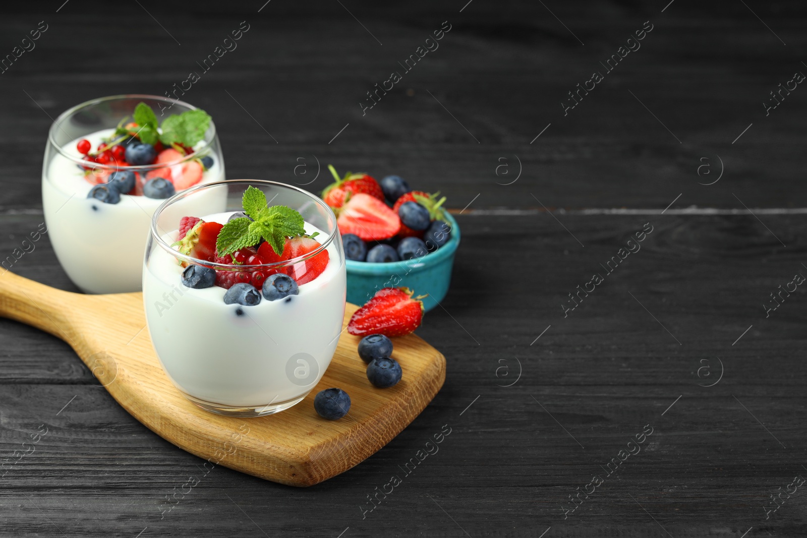 Photo of Tasty yogurt with fresh berries and mint in glasses on black wooden table, space for text