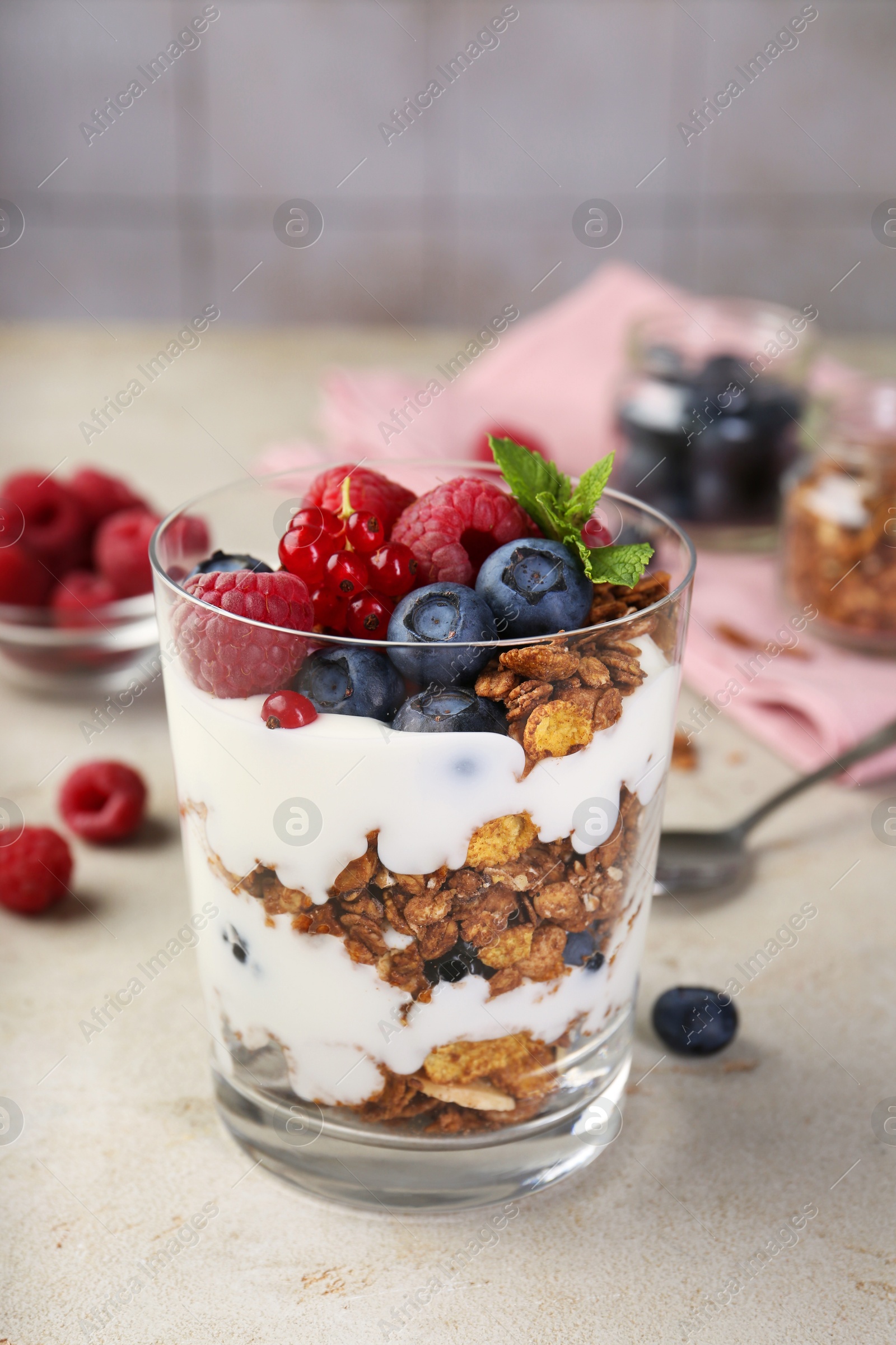 Photo of Tasty yogurt with fresh berries, granola and mint in glass on gray textured table