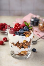 Photo of Tasty yogurt with fresh berries, granola and mint in glass on gray textured table