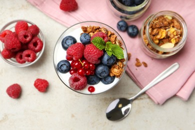 Photo of Tasty yogurt with fresh berries, granola, mint in glass and spoon on gray textured table, flat lay