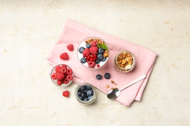 Photo of Tasty yogurt with fresh berries, granola, mint in glass and spoon on gray textured table, flat lay