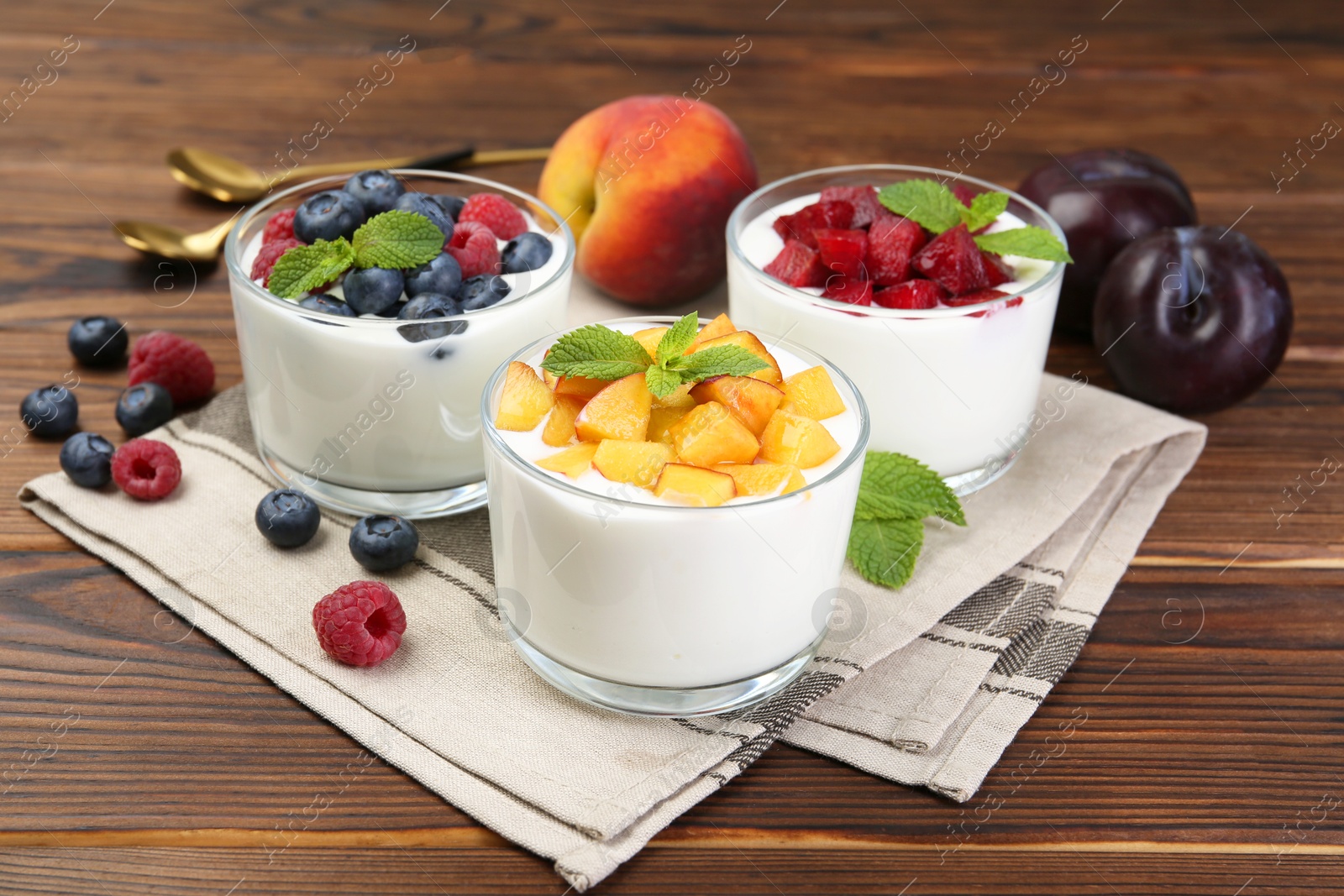 Photo of Tasty yogurt with fresh berries, fruits and mint in glasses on wooden table, closeup