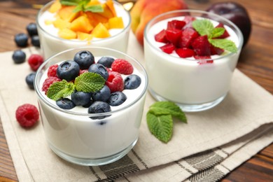 Photo of Tasty yogurt with fresh berries, fruits and mint in glasses on wooden table, closeup