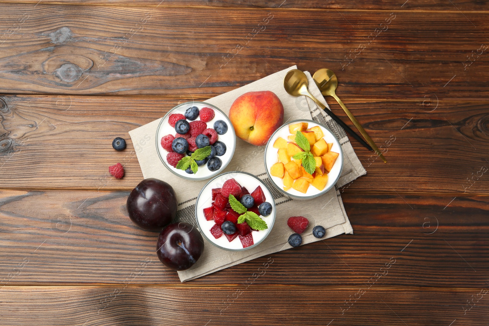 Photo of Tasty yogurt with fresh berries, fruits, mint in glasses and spoons on wooden table, flat lay