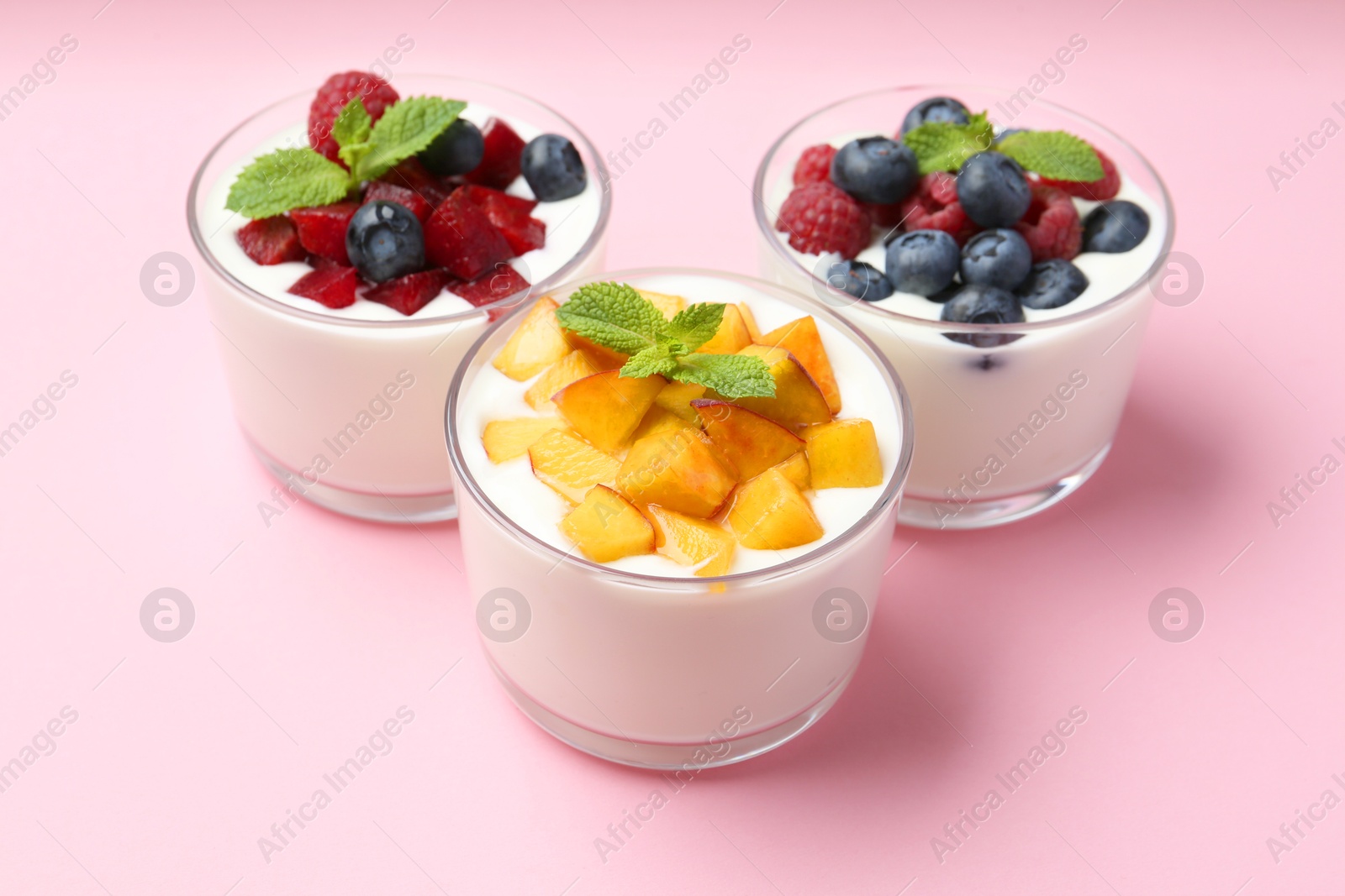 Photo of Tasty yogurt with fresh berries, fruits and mint in glasses on pink background, closeup