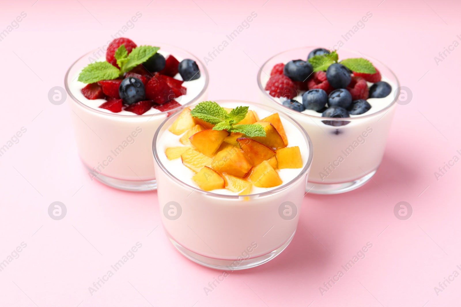 Photo of Tasty yogurt with fresh berries, fruits and mint in glasses on pink background, closeup