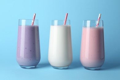 Different tasty yogurts and straws in glasses on light blue background