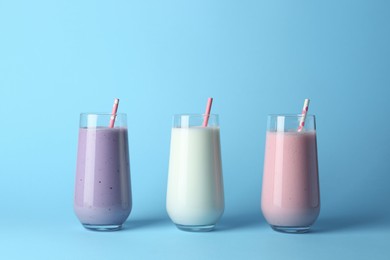 Photo of Different tasty yogurts and straws in glasses on light blue background