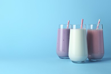 Different tasty yogurts and straws in glasses on light blue background, space for text