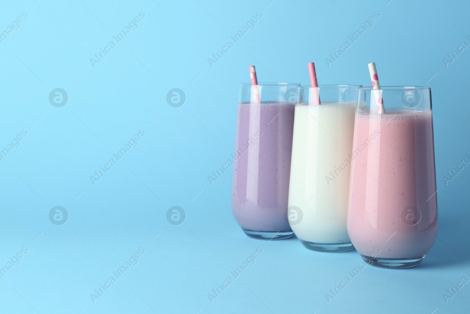 Photo of Different tasty yogurts and straws in glasses on light blue background, space for text