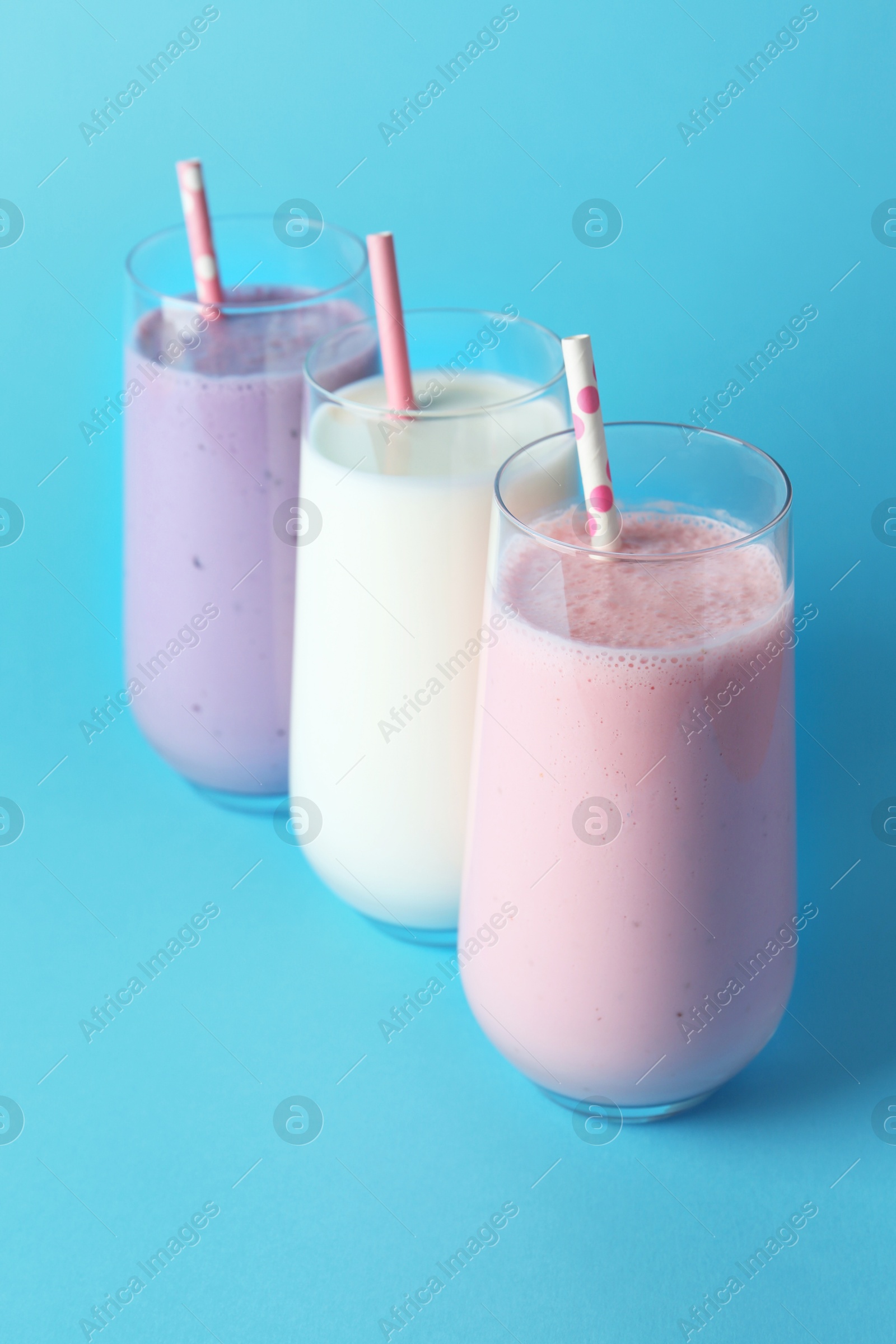 Photo of Different tasty yogurts and straws in glasses on light blue background, closeup