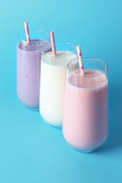 Photo of Different tasty yogurts and straws in glasses on light blue background, closeup