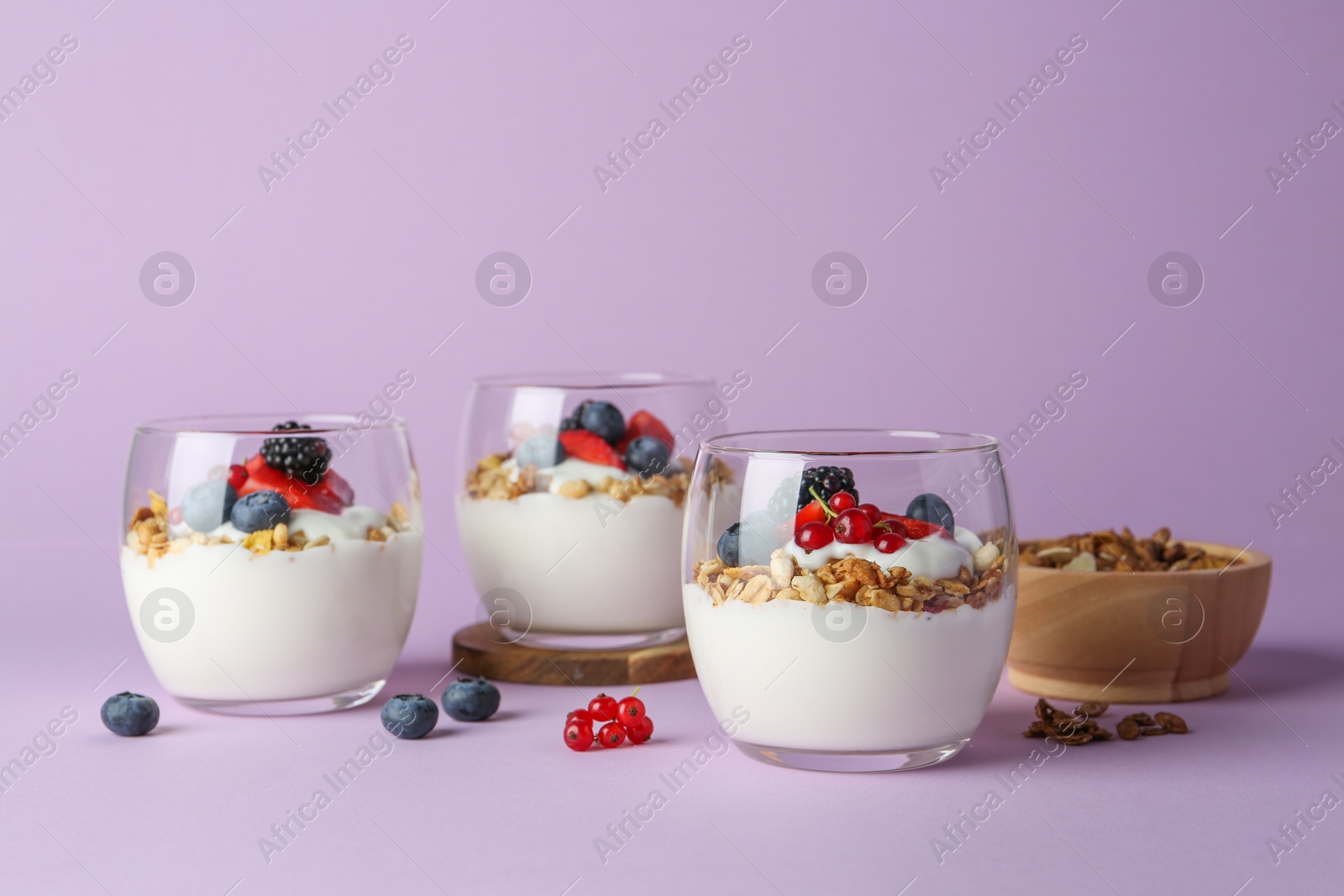 Photo of Tasty yogurt with fresh berries and granola in glasses on violet background