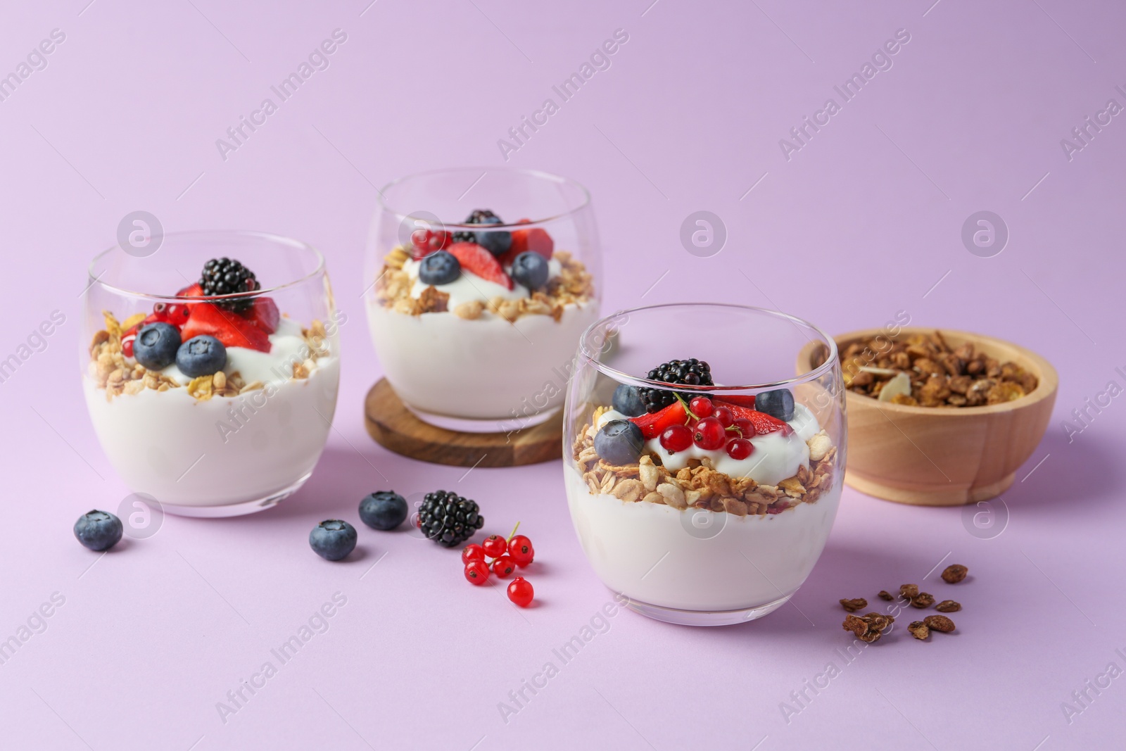 Photo of Tasty yogurt with fresh berries and granola in glasses on violet background