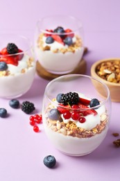 Photo of Tasty yogurt with fresh berries and granola in glasses on violet background, closeup