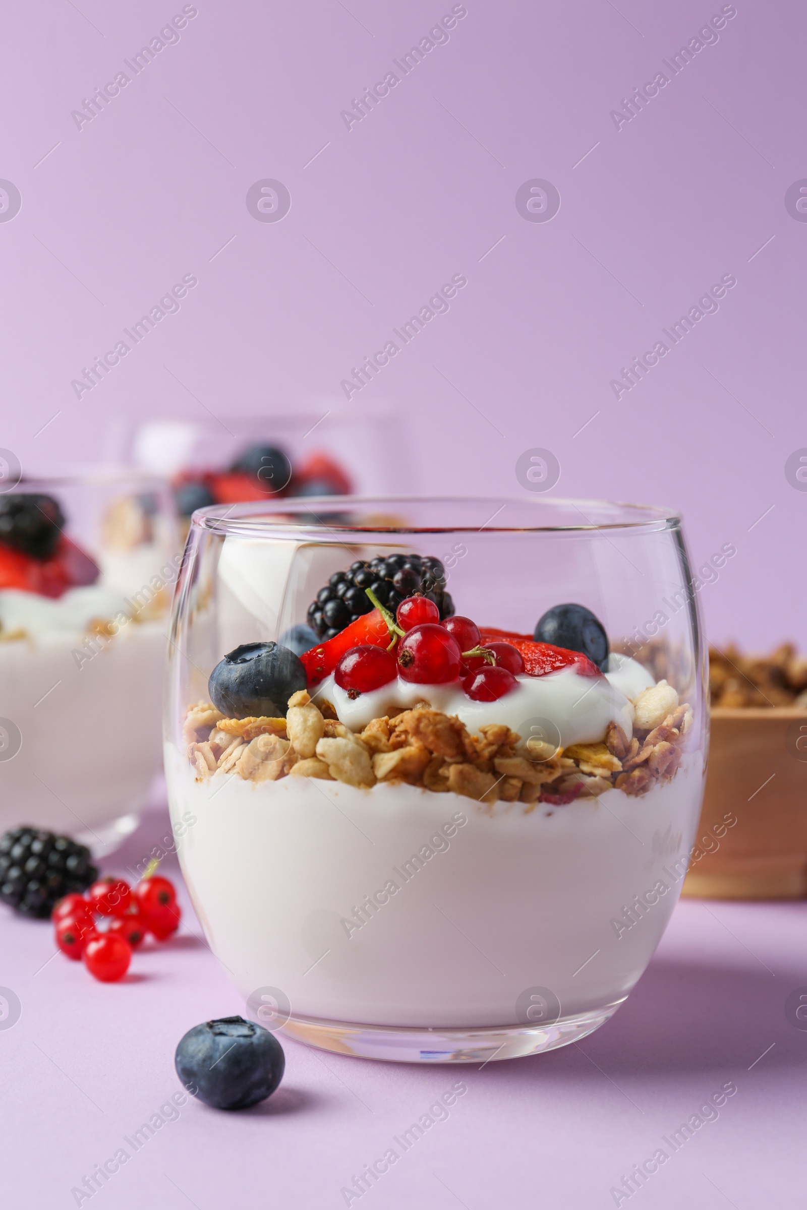 Photo of Tasty yogurt with fresh berries and granola in glass on violet background