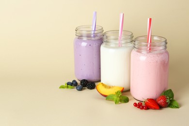 Photo of Different tasty yogurts in mason jars, peach, fresh berries and mint on pale yellow background, space for text