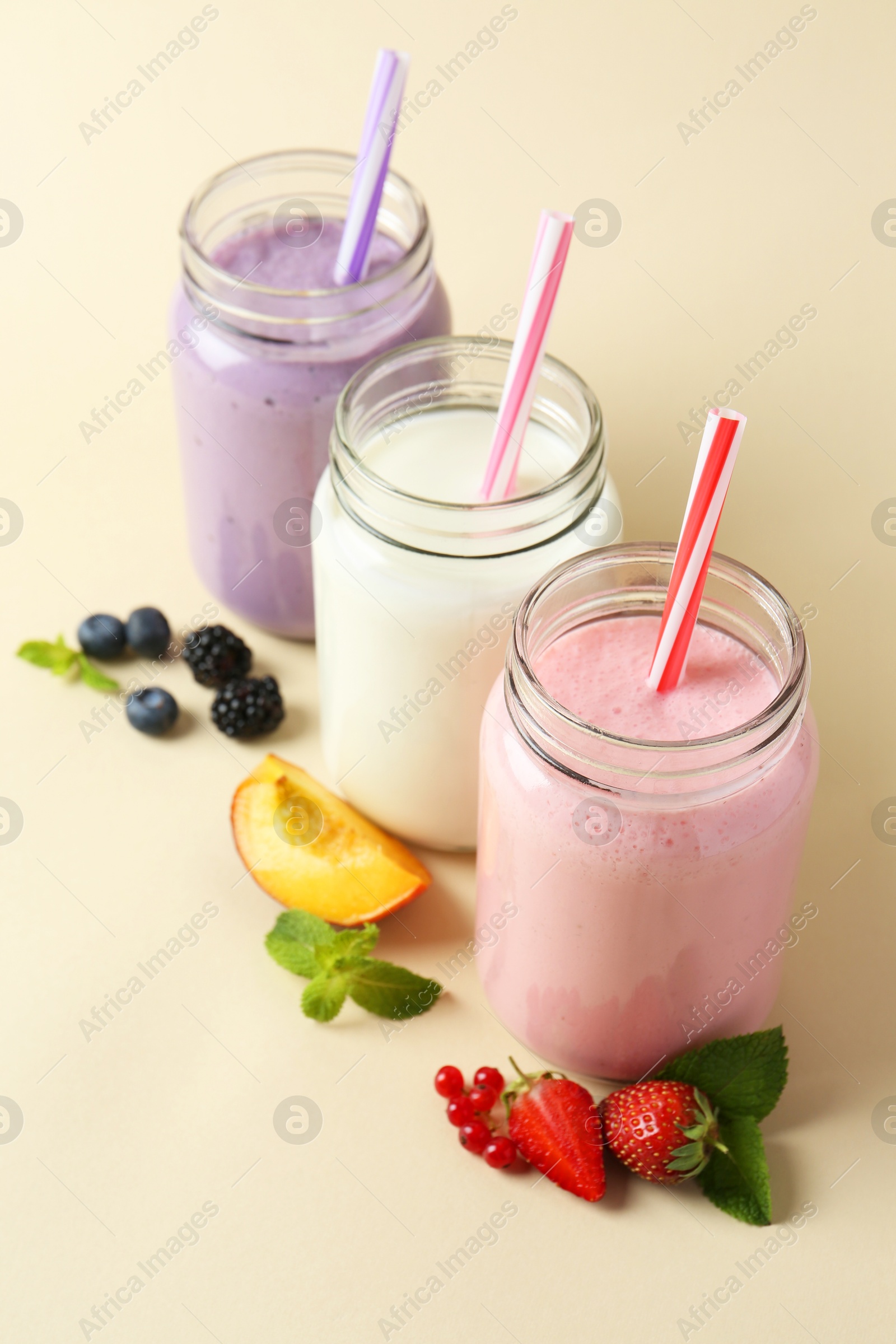 Photo of Different tasty yogurts in mason jars, peach, fresh berries and mint on pale yellow background, closeup