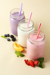 Photo of Different tasty yogurts in mason jars, peach, fresh berries and mint on pale yellow background, closeup