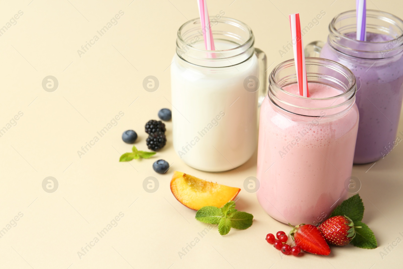 Photo of Different tasty yogurts in mason jars, peach, fresh berries and mint on pale yellow background, space for text