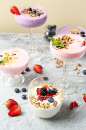 Photo of Different tasty yogurts with fresh berries and granola in glass dishware on gray textured table