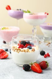 Photo of Different tasty yogurts with fresh berries and granola in glass dishware on gray textured table, closeup