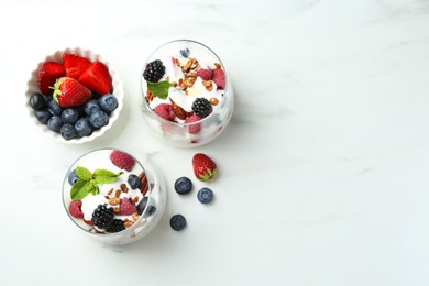 Photo of Tasty yogurt with fresh berries, granola and mint in glasses on white marble table, flat lay. Space for text