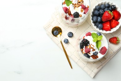 Photo of Tasty yogurt with fresh berries, granola and mint in glasses served on white table, flat lay. Space for text