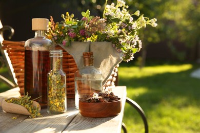 Photo of Different tinctures in bottles, bark chips and flowers on wooden bench outdoors