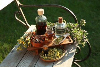 Different tinctures in bottles, bark chips and flowers on wooden bench outdoors