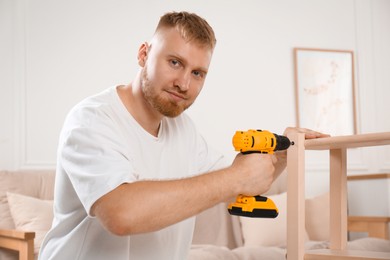 Photo of Man with electric screwdriver assembling furniture in room