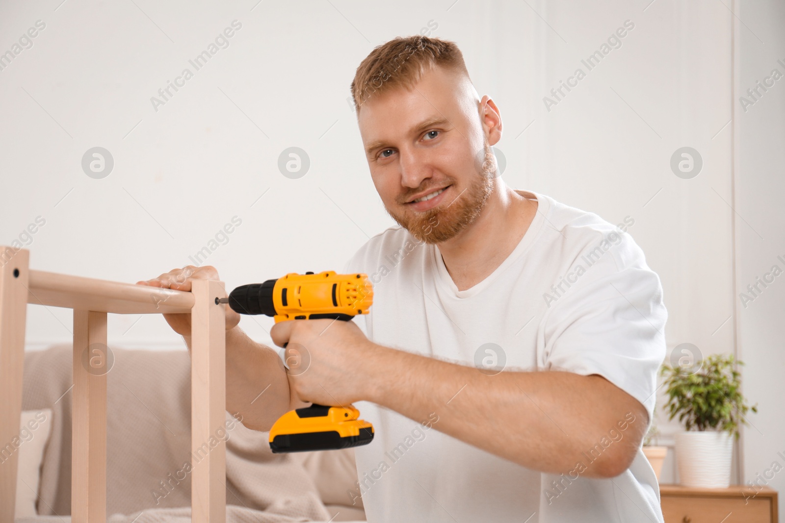 Photo of Man with electric screwdriver assembling furniture in room