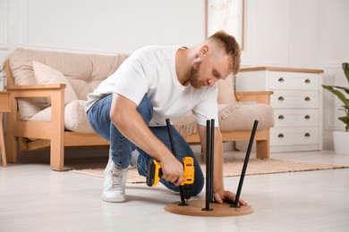 Photo of Man with electric screwdriver assembling table on floor in room