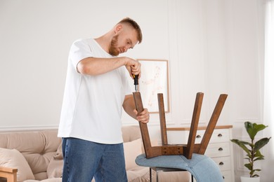 Man with screwdriver assembling chair in room