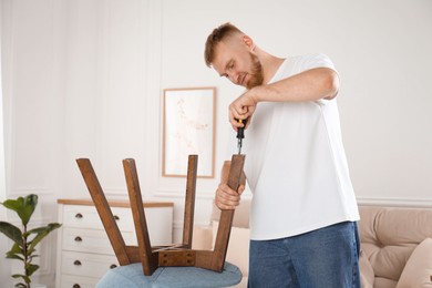 Man with screwdriver assembling chair in room