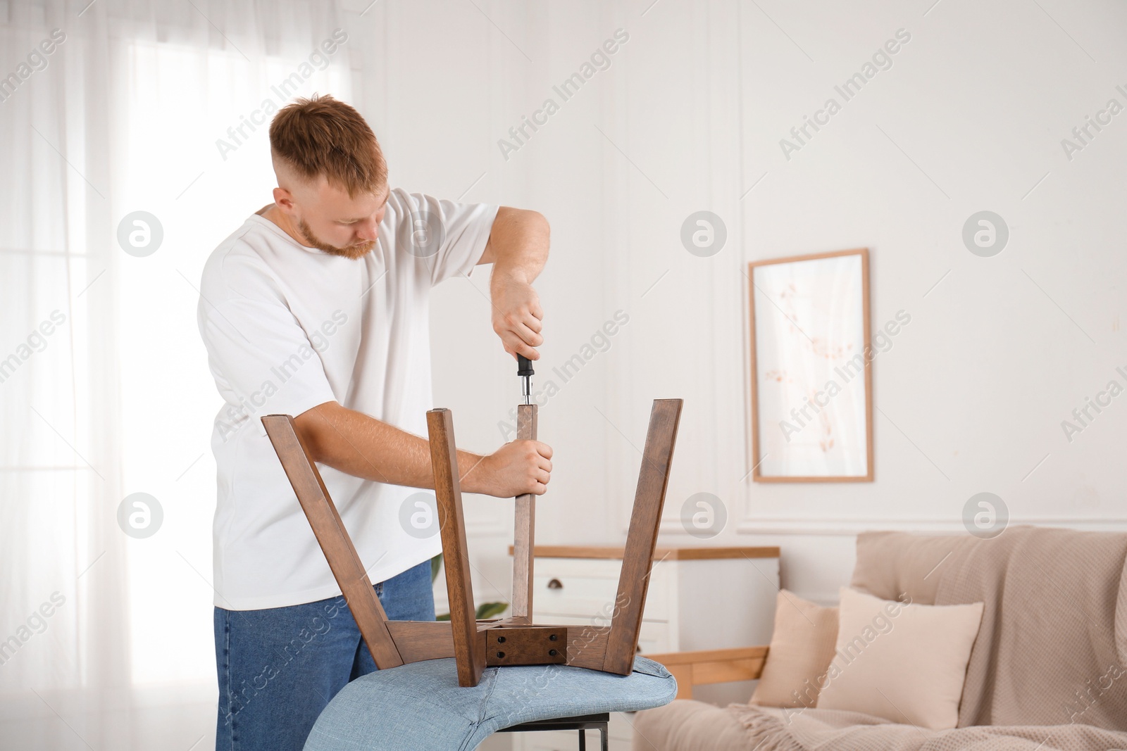 Photo of Man with screwdriver assembling chair in room