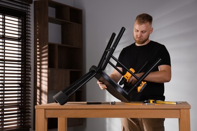 Photo of Man with electric screwdriver assembling chair in room