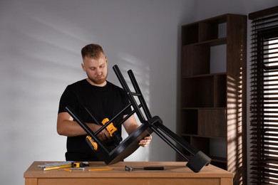 Photo of Man with electric screwdriver assembling chair in room