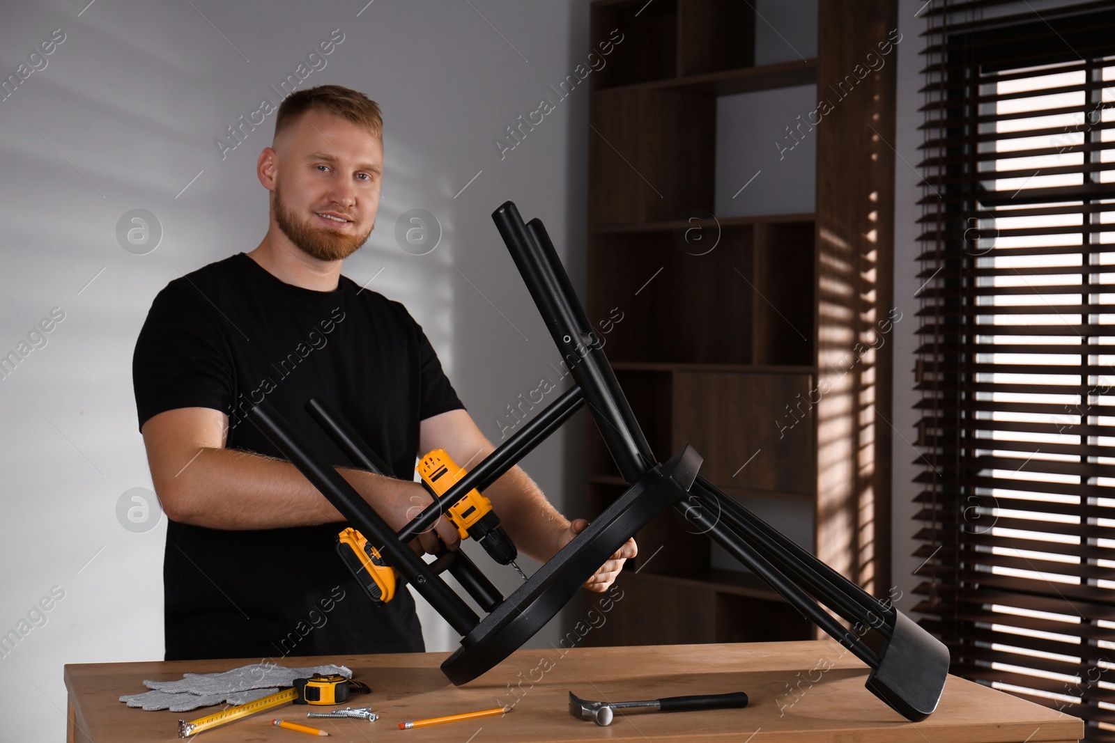 Photo of Man with electric screwdriver assembling chair in room