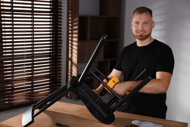 Photo of Man with electric screwdriver assembling chair in room