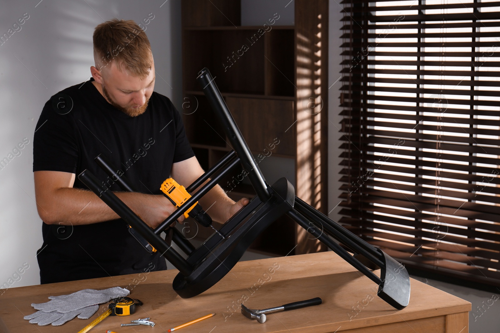 Photo of Man with electric screwdriver assembling chair in room