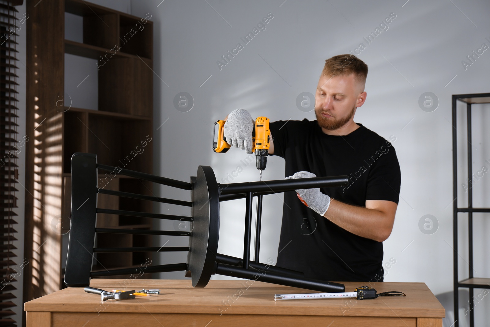 Photo of Man with electric screwdriver assembling chair in room