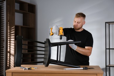 Man with electric screwdriver assembling chair in room