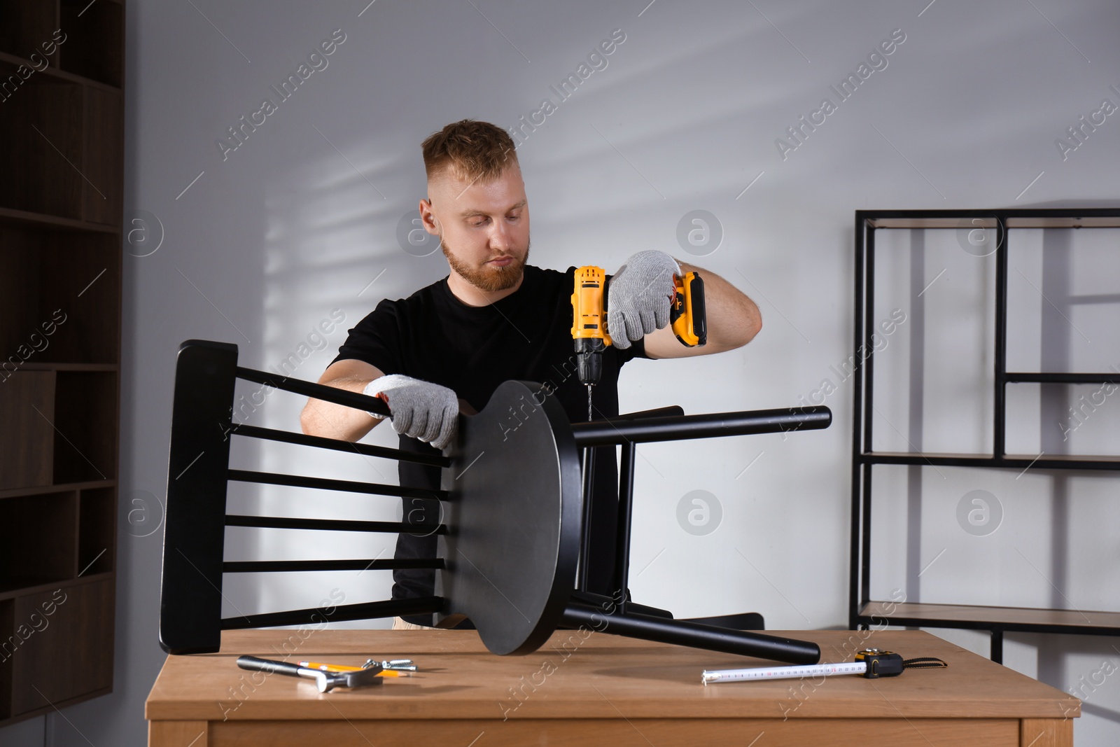 Photo of Man with electric screwdriver assembling chair in room