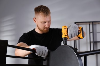 Photo of Man with electric screwdriver assembling chair in room